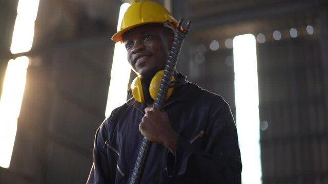 portrait of african american heavy industry worker wearing hard hat and yellow ear muffs standing confident  holding crowbar in Large Industrial Factory. young  black engineer