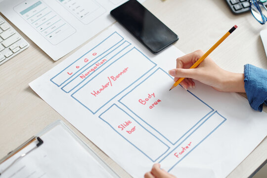 Hands of creative UI designer drawing mobile application interface layout on paper sheet