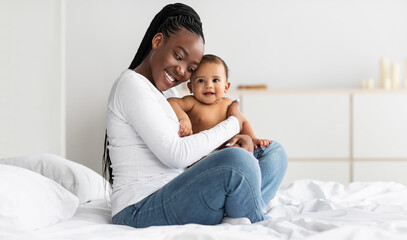 Black mom sitting on bed with her cute baby