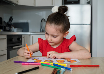 Younger schoolgirl draws Easter decorations and eggs at home in the kitchen. The girl herself draws and carves the decor for Easter.