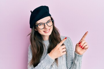 Young beautiful caucasian girl wearing french look with beret smiling and looking at the camera pointing with two hands and fingers to the side.