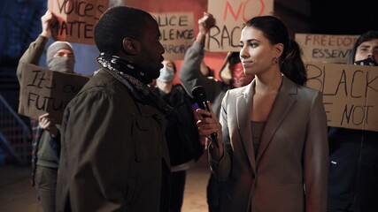 Caucasian female journalist interviewing African American aggressive male protester for news at...