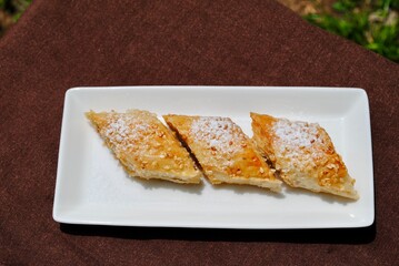 Homemade baklava on white rectangle plate on brown tablecloth. Turkish home baked sweet with seasame on top.