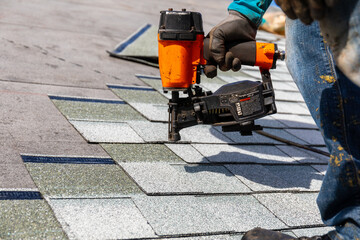 roofer installing roof shingles with nail gun - obrazy, fototapety, plakaty