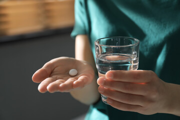 Young woman with abortion pill and glass of water indoors, closeup