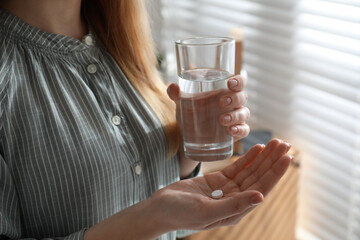 Young woman with abortion pill and glass of water indoors, closeup