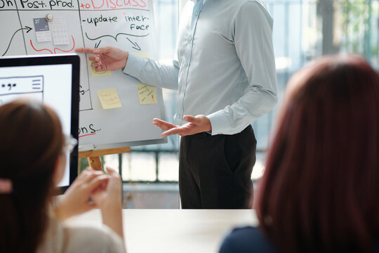 Cropped image of team leader pointing at whiteboard with notes and drawings at meeting with employees
