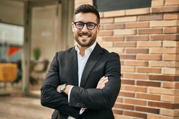 Young hispanic businessman with arms crossed smiling happy at the city.