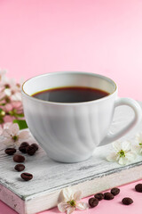 Cup of strong espresso coffee and delicate spring flowers on a pink background. Springtime and good morning concept.