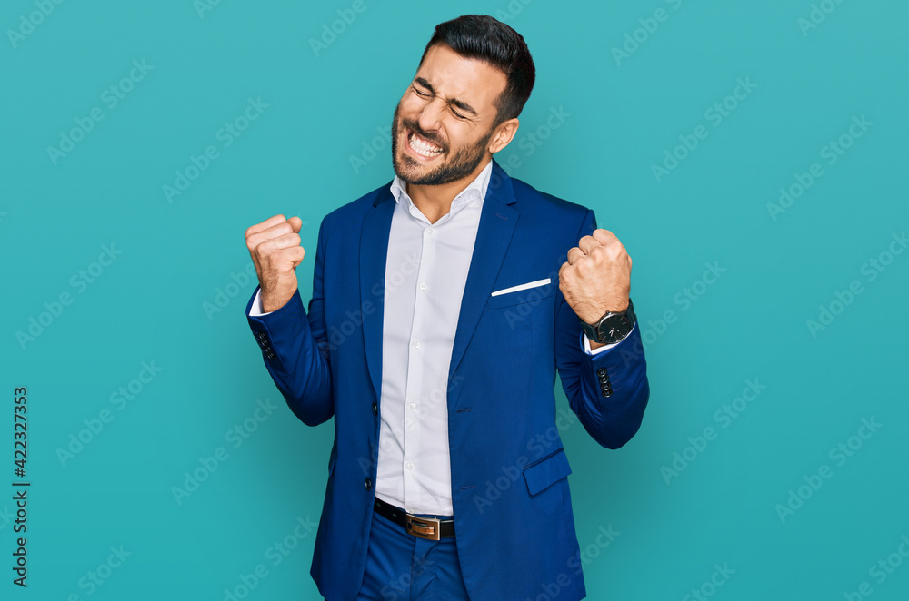 Sticker Young hispanic man wearing business jacket very happy and excited doing winner gesture with arms raised, smiling and screaming for success. celebration concept.