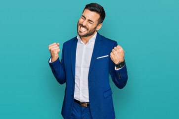 Young hispanic man wearing business jacket very happy and excited doing winner gesture with arms...