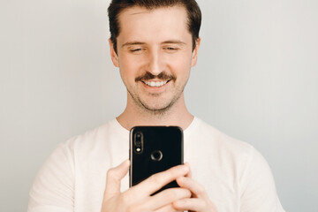 Young man smiles and looks into a mobile phone indoors. Live social media, mobile video calling, selfie concept