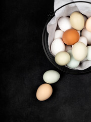 Fresh white chicken eggs in a metal basket with a napkin, top view, on a black textured background. Creativity.