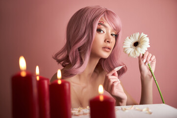 Beautiful woman with dyed pink hair guessing at flower in hand at table with candles. Pink beauty hair on head of woman fortune teller. Beauty Girl with flower in her hand