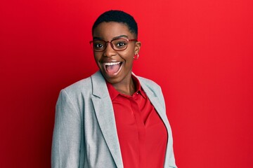 Young african american woman wearing business jacket and glasses winking looking at the camera with...