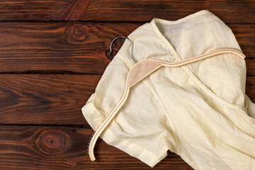 Light beige women's blouse and a plastic hanger on a wooden table with copy space. Top view.