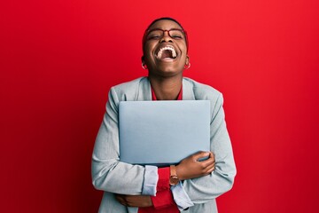 Young african american businesswoman holding laptop smiling and laughing hard out loud because funny crazy joke. - obrazy, fototapety, plakaty