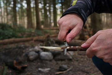 Caucasian male hand in winter jacket sharpening a wooden stick skewer with a nondescript pocket...