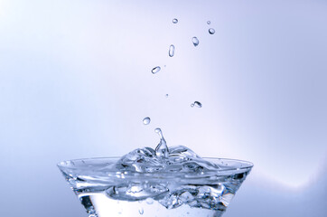 Close-up of water drop falling into a glass on white background