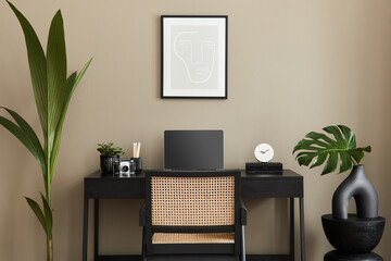 Modern interior design of home office space with stylish chair, desk, commode, black mock up poster frame, lapatop, book, desk organizer and elegant presonal accessories in home decor. Template.