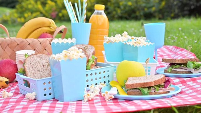 Lunch in the park on the green grass. Summer sunny day and picnic basket. Popcorn and sandwiches for a snack outdoors in nature. in bright plastic dishes . FullHD footage, Slow motion