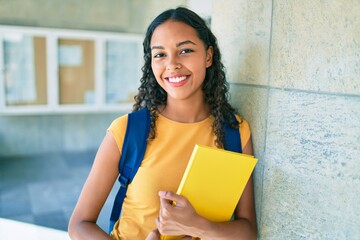 Young african american student smiling happy and holding book at university.
