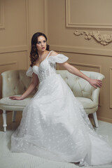 A beautiful bride is sitting in the studio on the couch in a lace dress. Sweet bride in a studio. Portrait of the bride.