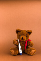 Teddy Bear is sick. Teddy bear toy and thermometer on a brown background with copy space.