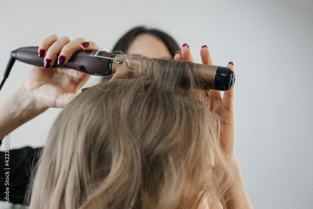 Wall mural master makes a hairstyle for a girl, beautiful curls