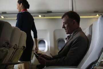 businessman in airliner working on his computer while talking by cellphone , Young handsome businessman with notebook sitting inside an airplane