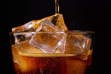 Fizz sparkling cola water refreshing bubbly soda pop with Ice cubes. Glass of cola on black background closeup.