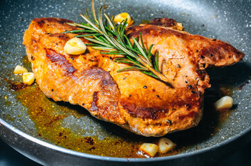 Delicious juicy pork steak seasoned with rosemary and garlic is fried in a pan.