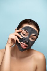 Beautiful young woman with mask for the face of black clay on clean fresh skin . Girl model beauty face care with moisturizer cosmetic mask  touches her face. Facial treatment . Skin care