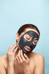 Beauty portrait woman skin care health black mask blue background close up. Girl  model  touches her face. Cosmetic mask .  Spa treatment . Cosmetology
