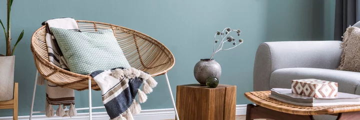 Fotobehang Boho Modern and bohemian composition of interior design with gray sofa, rattan armchair, wooden cube, plaid, pillow, flowers in vase, retro footrest and elegant accessories. Stylish home decor. Template.  © FollowTheFlow