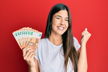 Young brunette woman holding 50 euro banknotes screaming proud, celebrating victory and success...