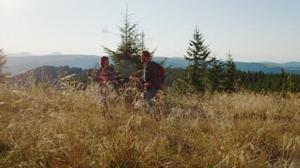 Obraz premium Smiling guy and girl hiking on road in field. Tourists trekking in mountains