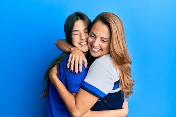 Beautiful hispanic mother and daughter smiling happy hugging over isolated blue background.