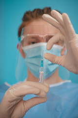 doctor in a sterile protective suit with a shield on his head prepares a syringe with a Covid-19 vaccine for an incoming patient. Medical worker. Fighting a pandemic. Blue tone