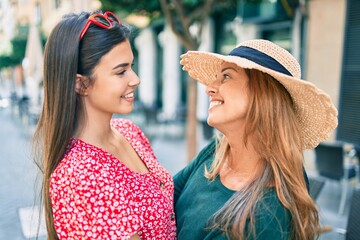 Beautiful hispanic mother and daughter on vacation smiling happy standing at the city.