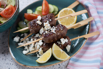 Turquoise plate with roasted greek kofta kebabs, feta cheese and fresh vegetables, selective focus, studio shot