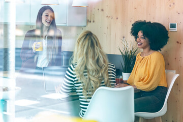 Three smart entrepreneur women talking while taking a break and having a breakfast in the kitchen at coworking place.