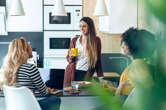 Three smart entrepreneur women talking while taking a break and having a breakfast in the kitchen at coworking place.