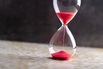 Sand passes through an hourglass, measuring the travel time counting down to the deadline, against...
