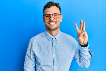 Young hispanic man wearing casual clothes and glasses showing and pointing up with fingers number three while smiling confident and happy.