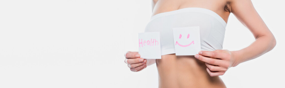 Cropped view of young woman in bra holding cards with smile sign and health lettering isolated on white, banner