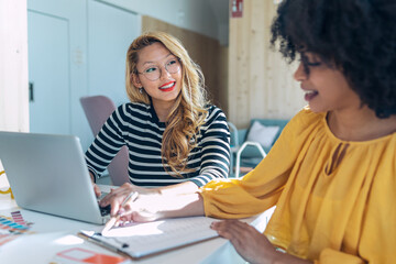 Casual multiethnic business women working with laptops while talking of they new projects together in coworking place.