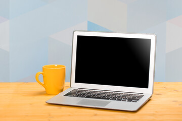 Laptop with blank screen for product display and cup of coffee on wooden table