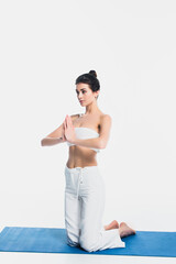 Brunette woman with praying hands practicing yoga on fitness mat isolated on white