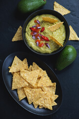 Above view of guacamole dip and corn chips over black stone background, vertical shot